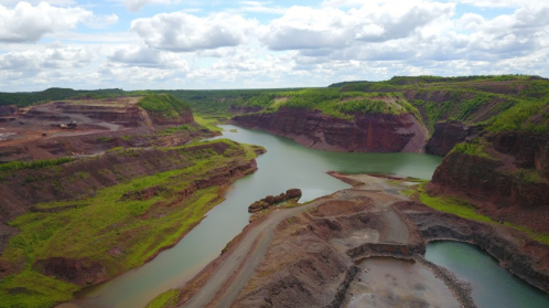 Aerial view of a lush green landscape with a winding river and steep, rocky cliffs under a cloudy sky.