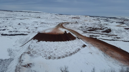 A snowy landscape with a winding dirt road and a large mound of earth, showcasing a mining or construction site.