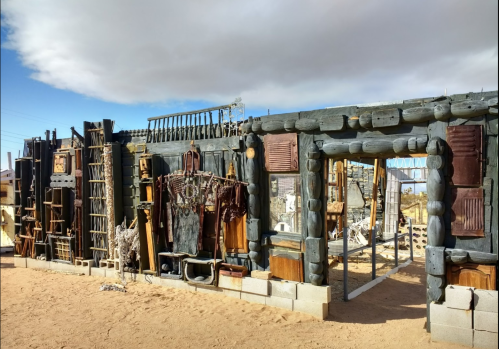 A unique, partially constructed building made of various materials, set against a desert landscape under a cloudy sky.