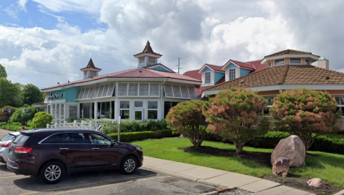 A restaurant with a colorful exterior and unique architecture, surrounded by greenery and a parked car in the foreground.