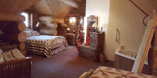Cozy log cabin bedroom with two beds, a Christmas tree, and a bathtub, featuring rustic wooden decor.