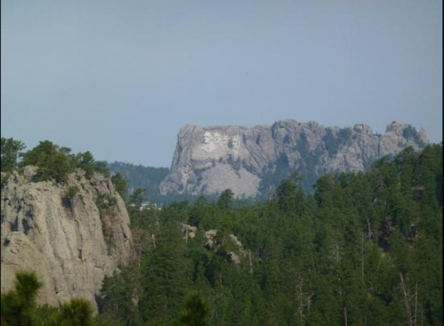 A distant view of a rocky mountain landscape with trees in the foreground and a prominent rock formation in the background.