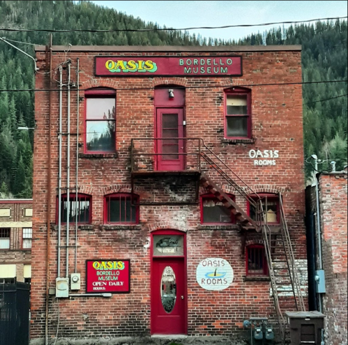 Historic brick building with signs for "Oasis Bordello Museum" and "Oasis Rooms," featuring a staircase and windows.