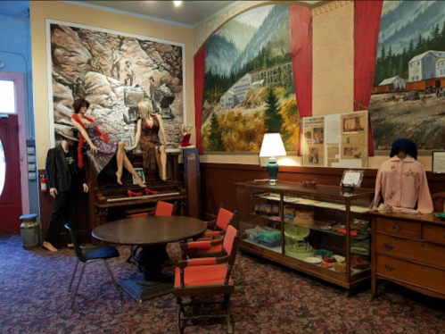 A vintage room with mannequins in period clothing, a round table, and historical murals on the walls.