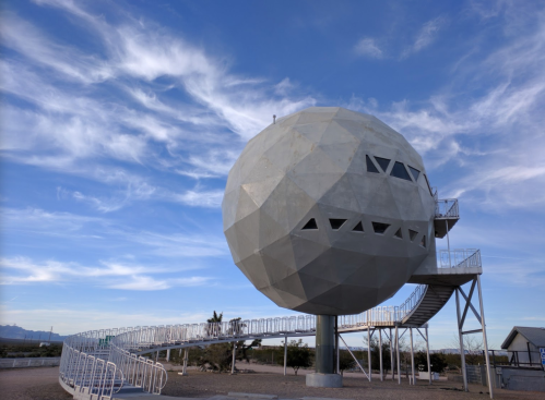 A large, spherical concrete structure on a raised platform, with a winding staircase and blue sky in the background.