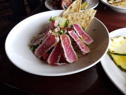 A bowl of seared tuna slices on a bed of mixed greens, garnished with cucumber and served with flatbread.