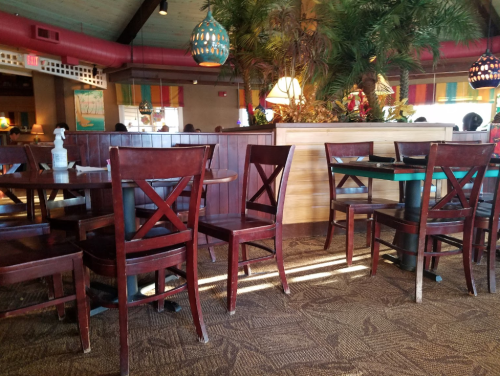 Interior of a restaurant featuring wooden tables and chairs, with tropical decor and plants in the background.