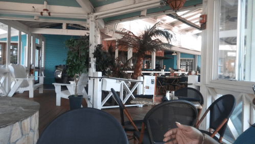 Interior of a bright, tropical-themed restaurant with wooden furniture and plants, featuring empty tables and chairs.