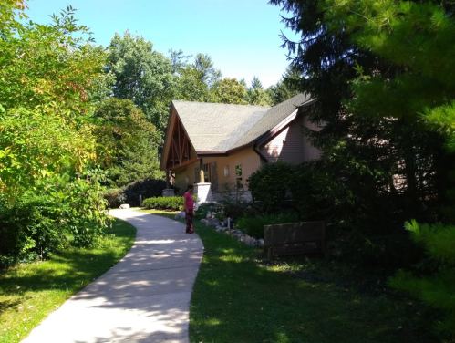 A pathway leads to a house surrounded by trees and greenery, with a person standing near the entrance.