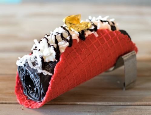 A red waffle cone filled with chocolate ice cream, topped with whipped cream, chocolate drizzle, and a gold decoration.