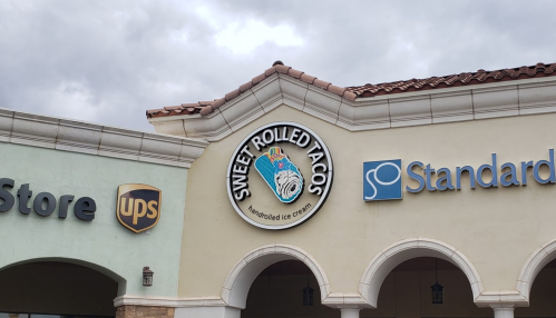 Sign for "Sweet Rolled Tacos" featuring a colorful ice cream cone, located above storefronts with UPS and Standard logos.