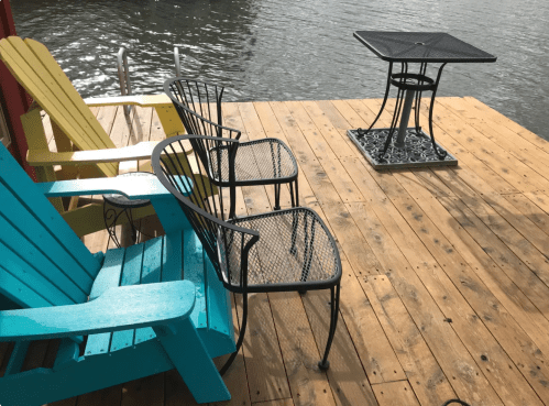 A wooden deck by the water featuring colorful chairs and a table, creating a relaxing outdoor space.