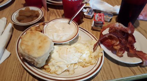 A plate of breakfast featuring eggs, biscuits, gravy, hash browns, bacon, and a side of fruit.