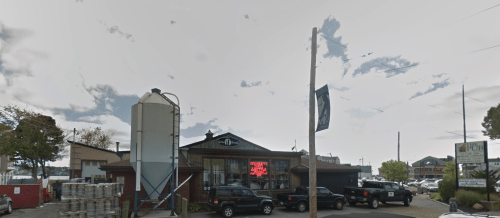 A pub with a large sign, surrounded by parked trucks and a silos, under a cloudy sky.