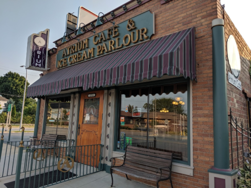 Exterior of Atrium Café & Ice Cream Parlour, featuring a striped awning and wooden benches outside.