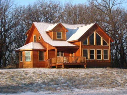 A cozy wooden house with a snow-dusted roof, surrounded by trees in a winter landscape.