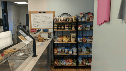 A snack display featuring various packaged snacks on shelves next to a counter with a menu board.