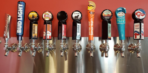 A row of colorful beer taps featuring various brands and designs against a red wall.