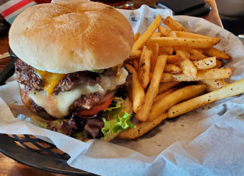A juicy burger with cheese, lettuce, and tomato, served with a side of crispy fries in a basket.