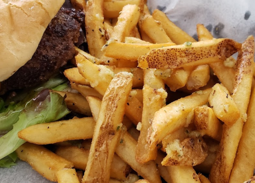 A close-up of golden, crispy French fries next to a burger and lettuce on a tray.