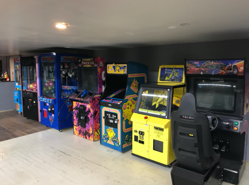 A row of vintage arcade machines in a game room, featuring various colorful cabinets and a racing game setup.