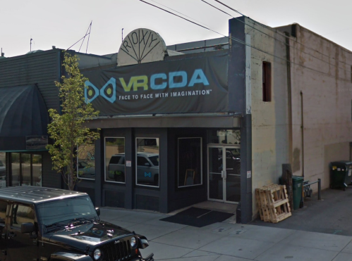 Exterior of a building with a sign for "VRCD" and the tagline "Face to Face with Imagination." A black vehicle is parked nearby.