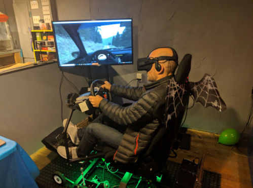A person wearing a VR headset drives a racing simulator with a monitor displaying a mountain road.