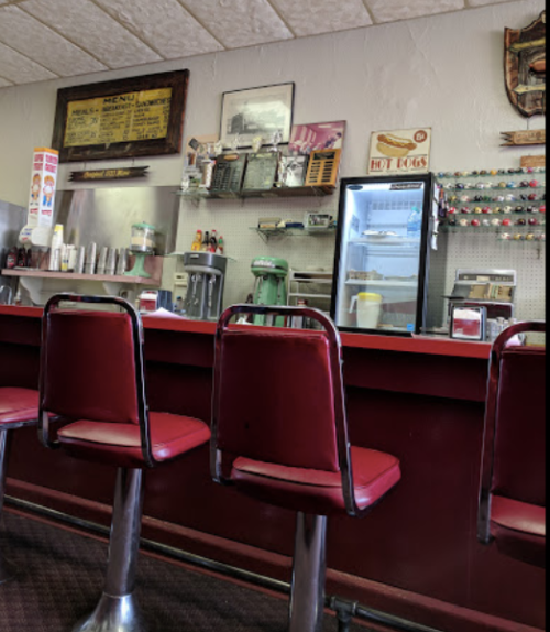 A retro diner interior featuring red stools at a counter, vintage decor, and a display fridge.