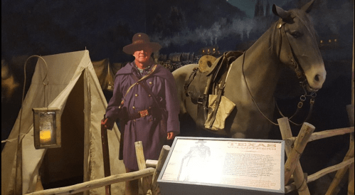 A historical exhibit featuring a soldier in uniform beside a horse and a tent, with a sign reading "Texas Volunteers."