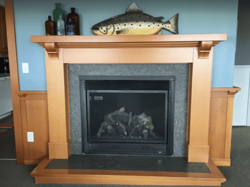 A wooden fireplace mantel with a decorative fish and bottles on top, featuring a modern black fireplace below.