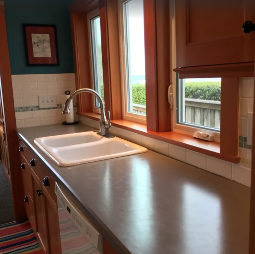 Bright kitchen with a white sink, wooden cabinets, and large windows overlooking a garden.
