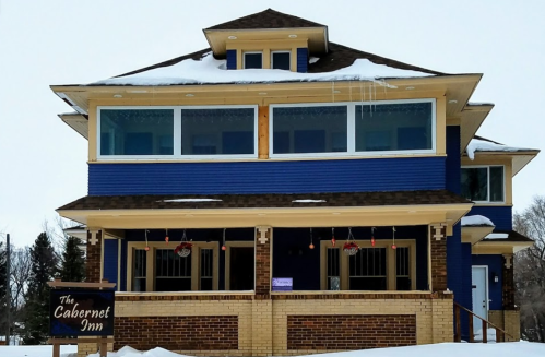 A blue and tan inn with multiple stories, snow on the ground, and festive decorations on the windows.