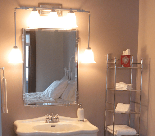 A modern bathroom with a stylish mirror, sink, and a towel rack holding neatly stacked towels. Soft lighting enhances the space.