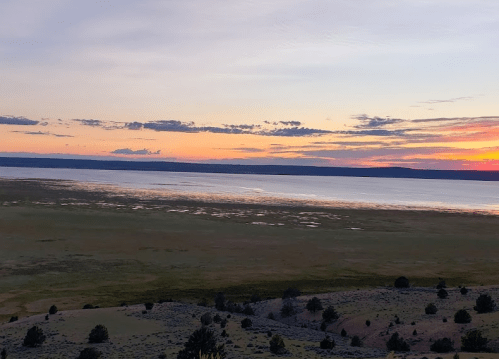 A serene landscape at sunset, featuring a calm lake and distant mountains under a colorful sky.