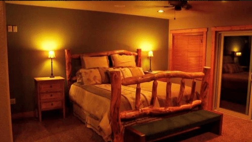 Cozy bedroom with a log bed, bedside lamps, and a sliding glass door, featuring warm lighting and rustic decor.