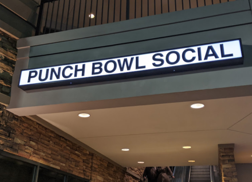 Sign for "Punch Bowl Social" illuminated above a building entrance, with a modern design and stone wall background.