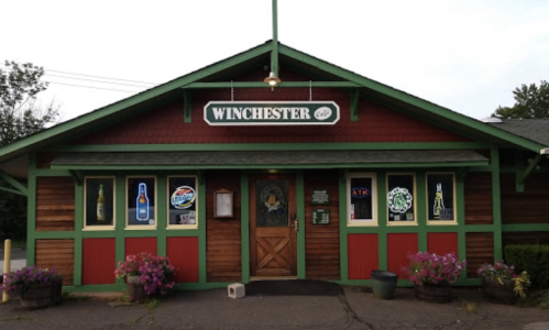 Exterior of the Winchester Cafe, featuring a wooden facade, colorful signage, and flower planters at the entrance.