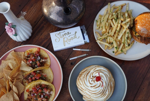 A table spread featuring tacos, fries, a burger, and a dessert, with a decorative vase and a business card.