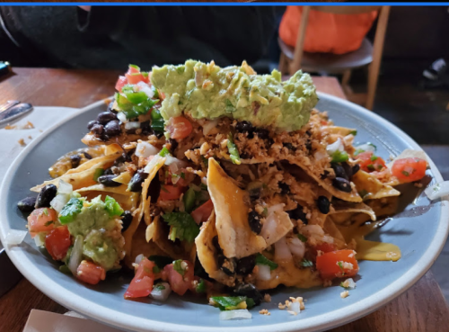 A plate of nachos topped with cheese, black beans, guacamole, pico de gallo, and crispy toppings.