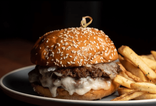 A juicy cheeseburger with melted cheese on a sesame seed bun, served with crispy French fries on the side.