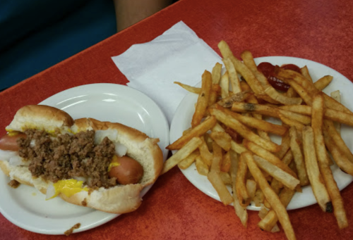 A plate with a hot dog topped with ground beef and cheese, alongside a serving of crispy French fries.