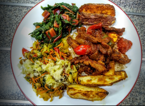 A plate of food featuring rice, sautéed beef with peppers, fried plantains, and two types of sautéed greens.