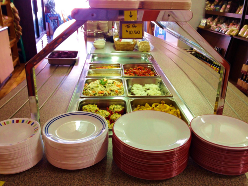 A buffet setup with various dishes in metal trays and stacks of plates ready for serving.