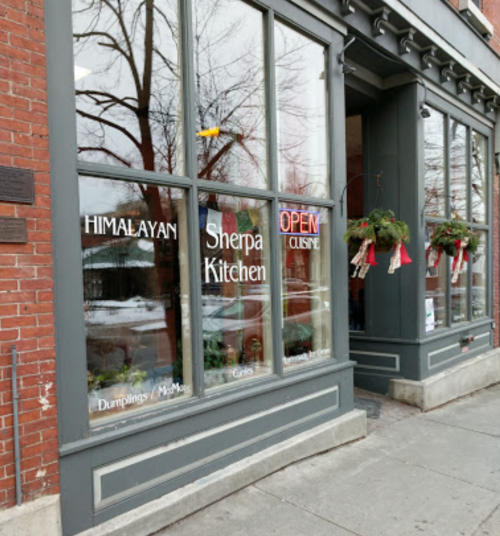 Exterior of a restaurant named "Himalayan Sherpa Kitchen," featuring large windows and festive decorations.
