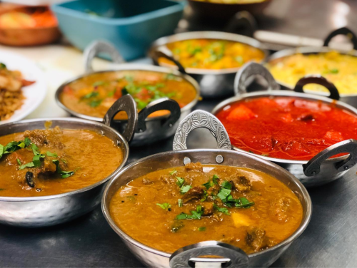 A variety of colorful curries in metal bowls, garnished with herbs, arranged on a table.