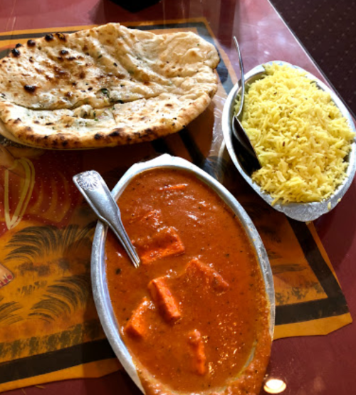 A plate of paneer curry with naan bread and a side of yellow rice on a colorful table.
