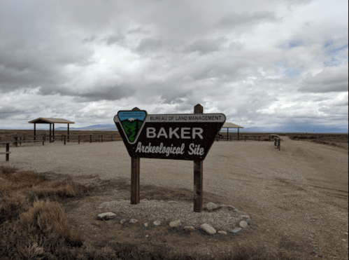 Sign for Baker Archaeological Site, with cloudy skies and open landscape in the background.