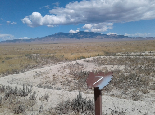 A metal marker with the number 7 in a barren landscape, with mountains and clouds in the background.