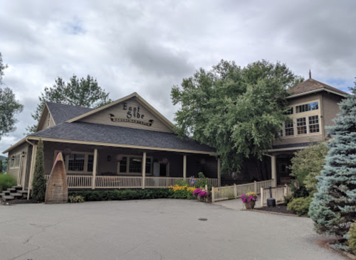 A charming restaurant with a wooden exterior, surrounded by trees and colorful flowers under a cloudy sky.
