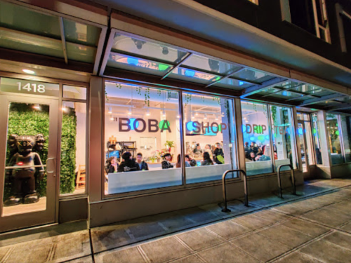 A brightly lit boba shop with large windows, showcasing customers inside and colorful signage.